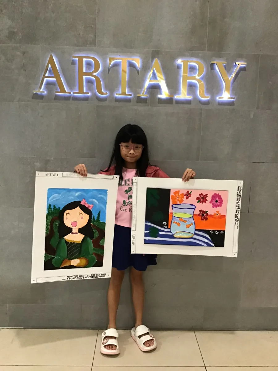Child holding a painted portrait and a colourful fish-jug picture.
